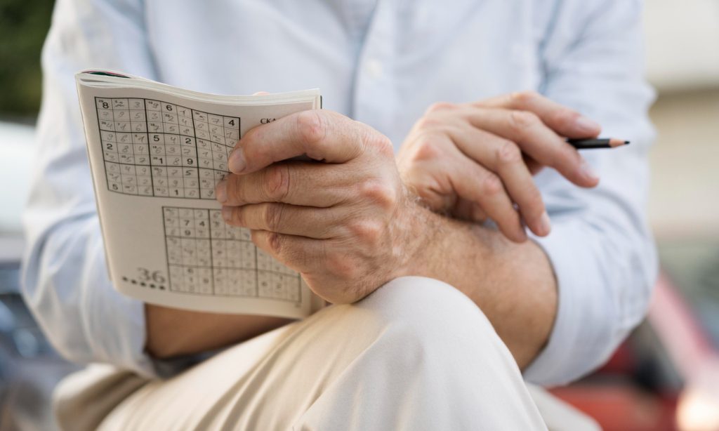 old person holding a sudoku puzzle book