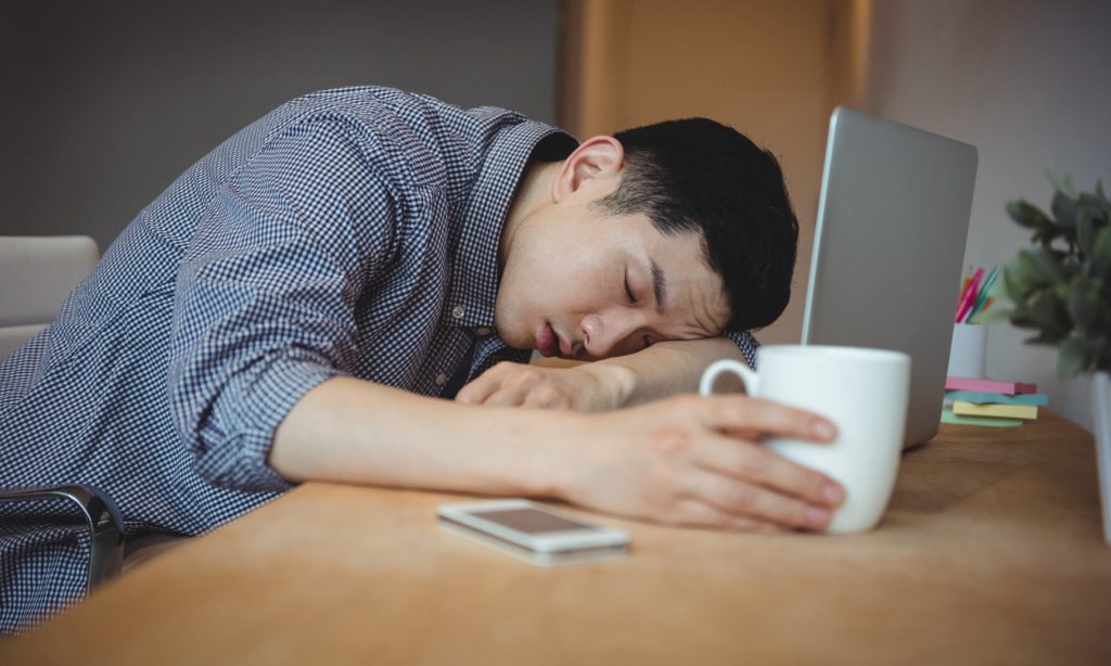 man taking a nap while working holding a mug