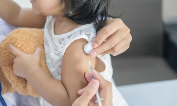 toddler receiving vaccination while holding teddy bear